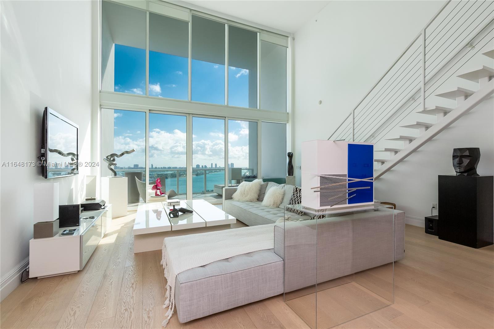 Modern living room with floor-to-ceiling windows overlooking water and a distant city skyline.