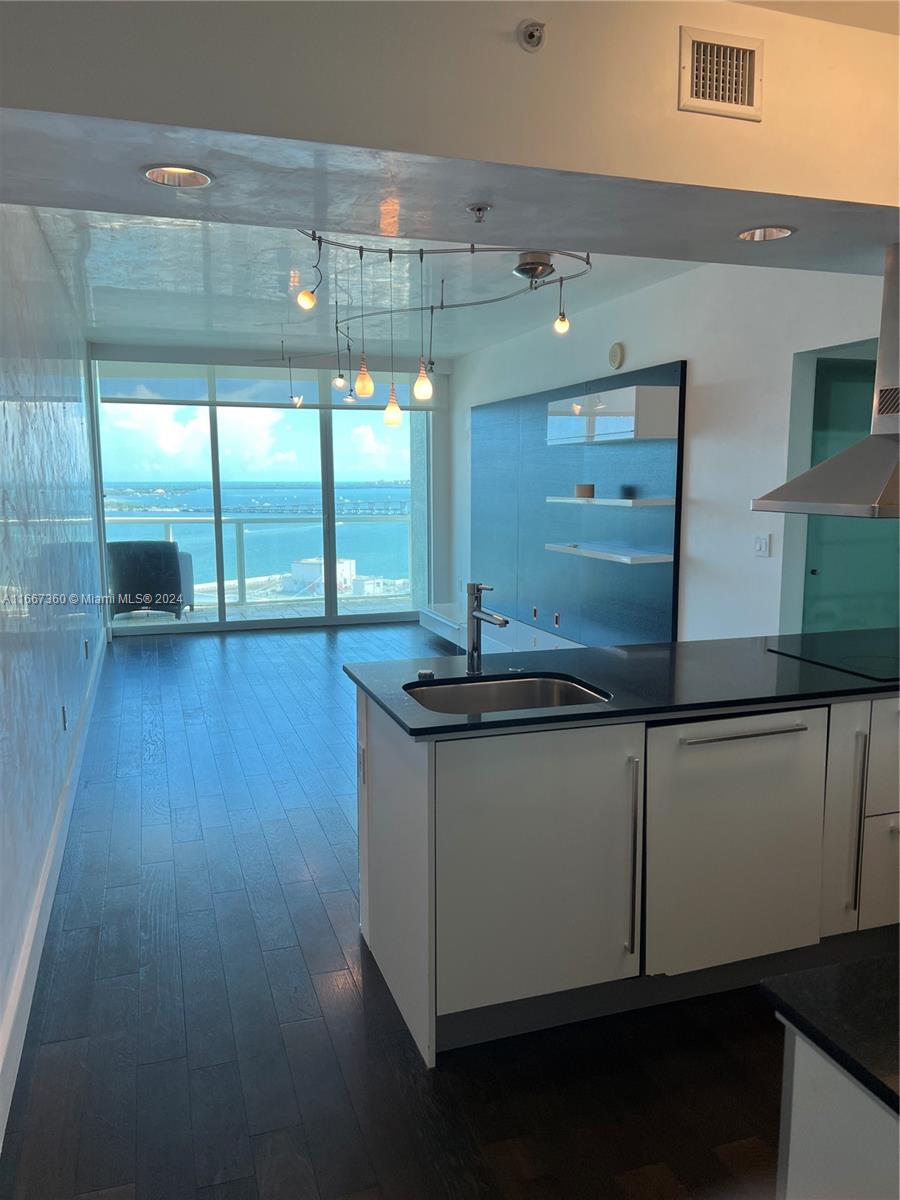 Modern condo kitchen opens toward floor-to-ceiling windows overlooking the water.
