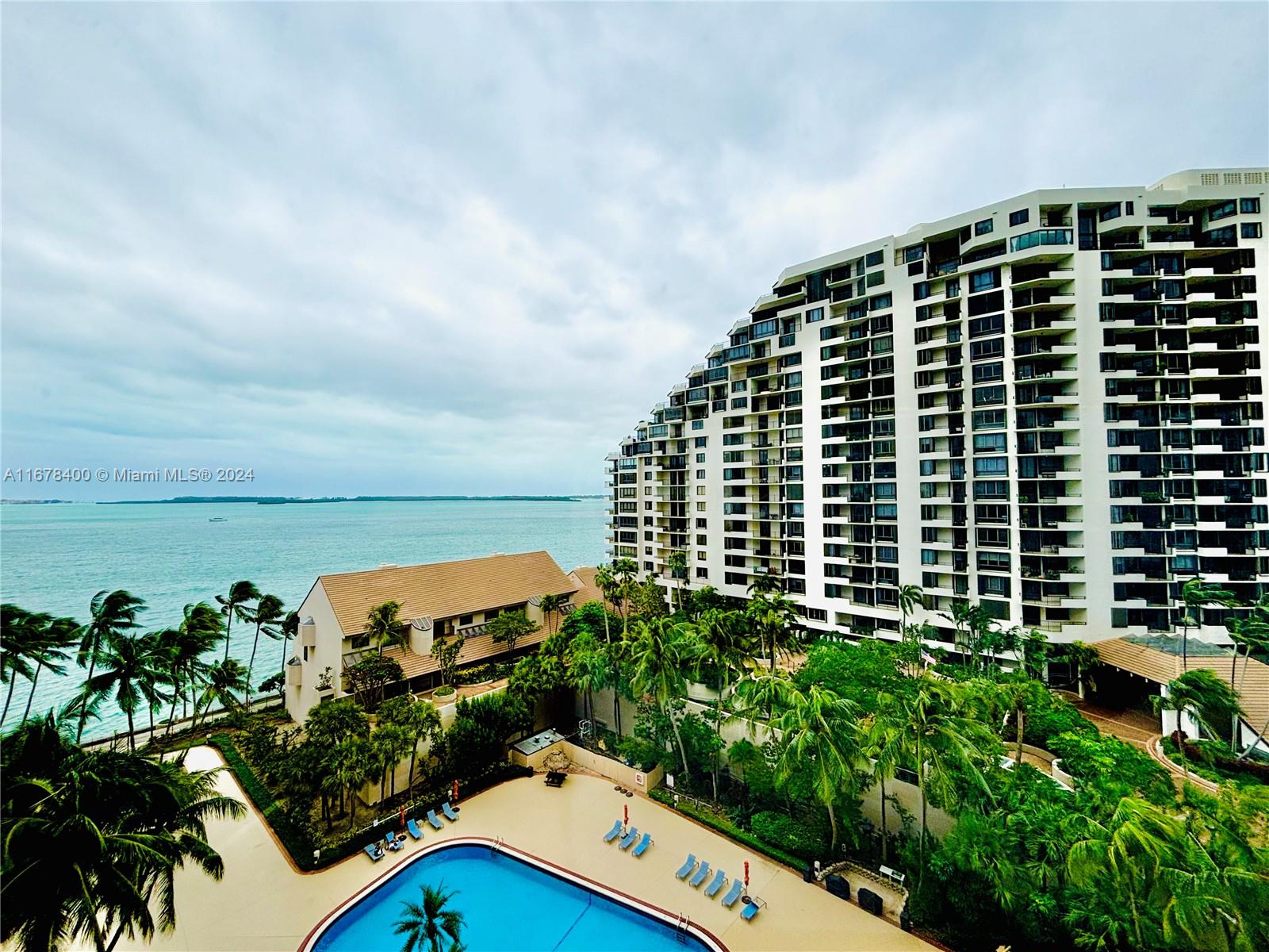 Waterfront condominium tower overlooking the bay, with a palm-lined pool below.