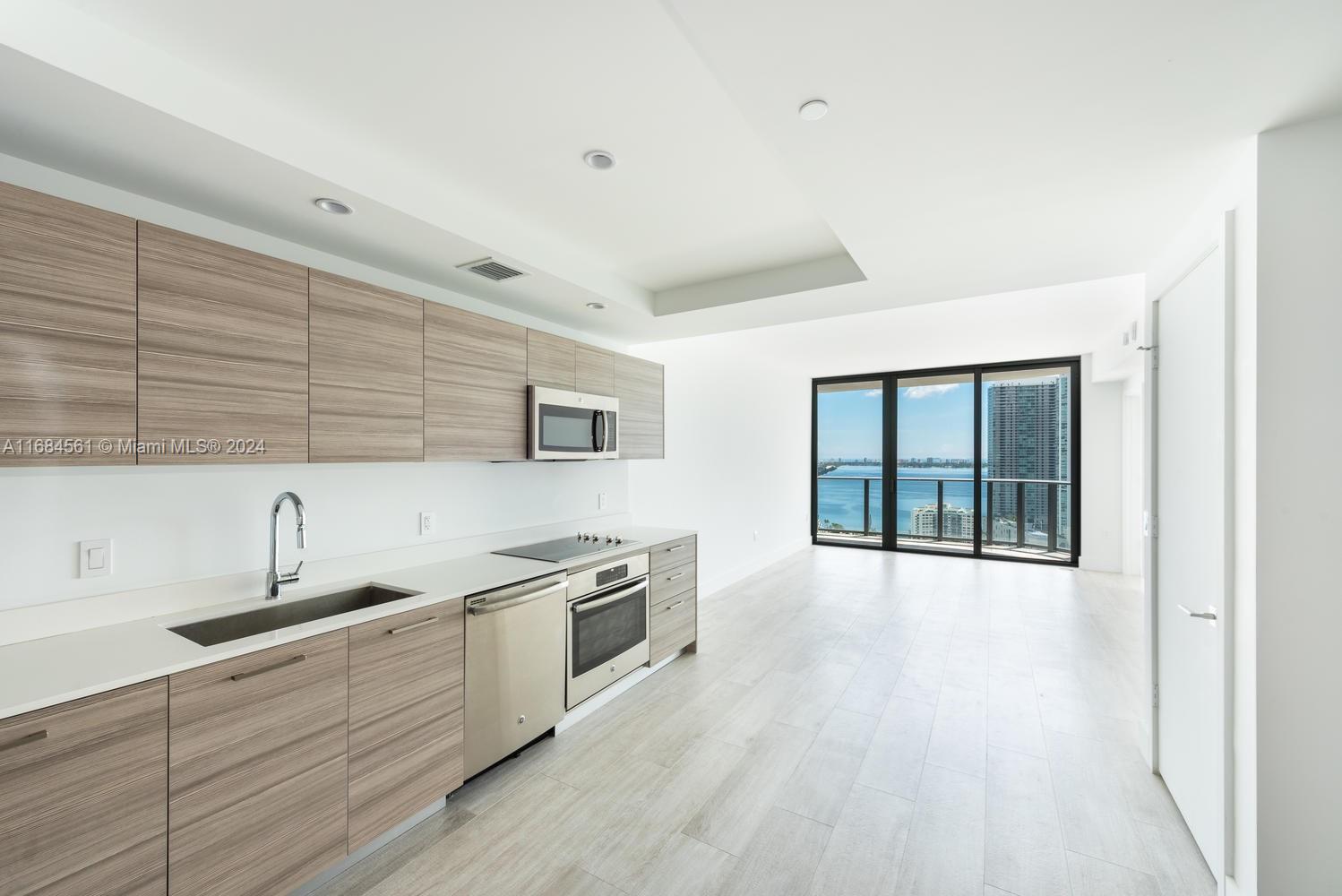 Modern apartment kitchen with wood-grain cabinets and views of the water and city skyline.