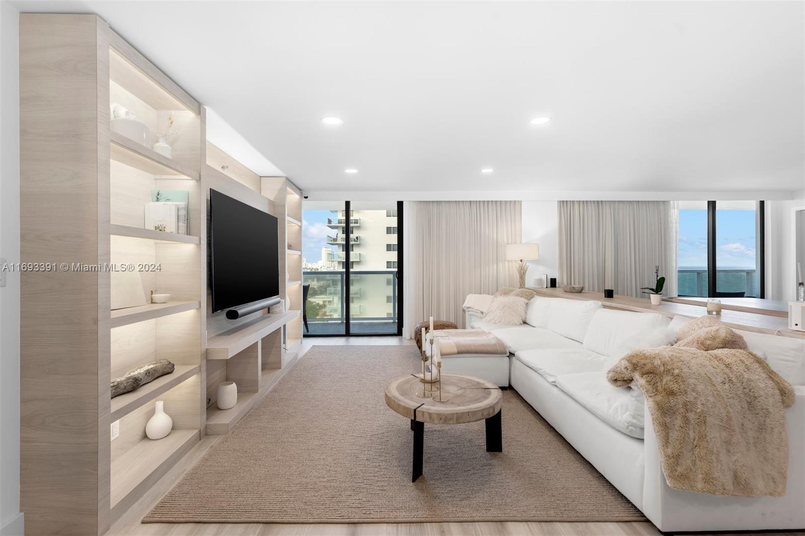 Bright living room with a white sectional, built-in shelving, and ocean views through floor-to-ceiling windows.