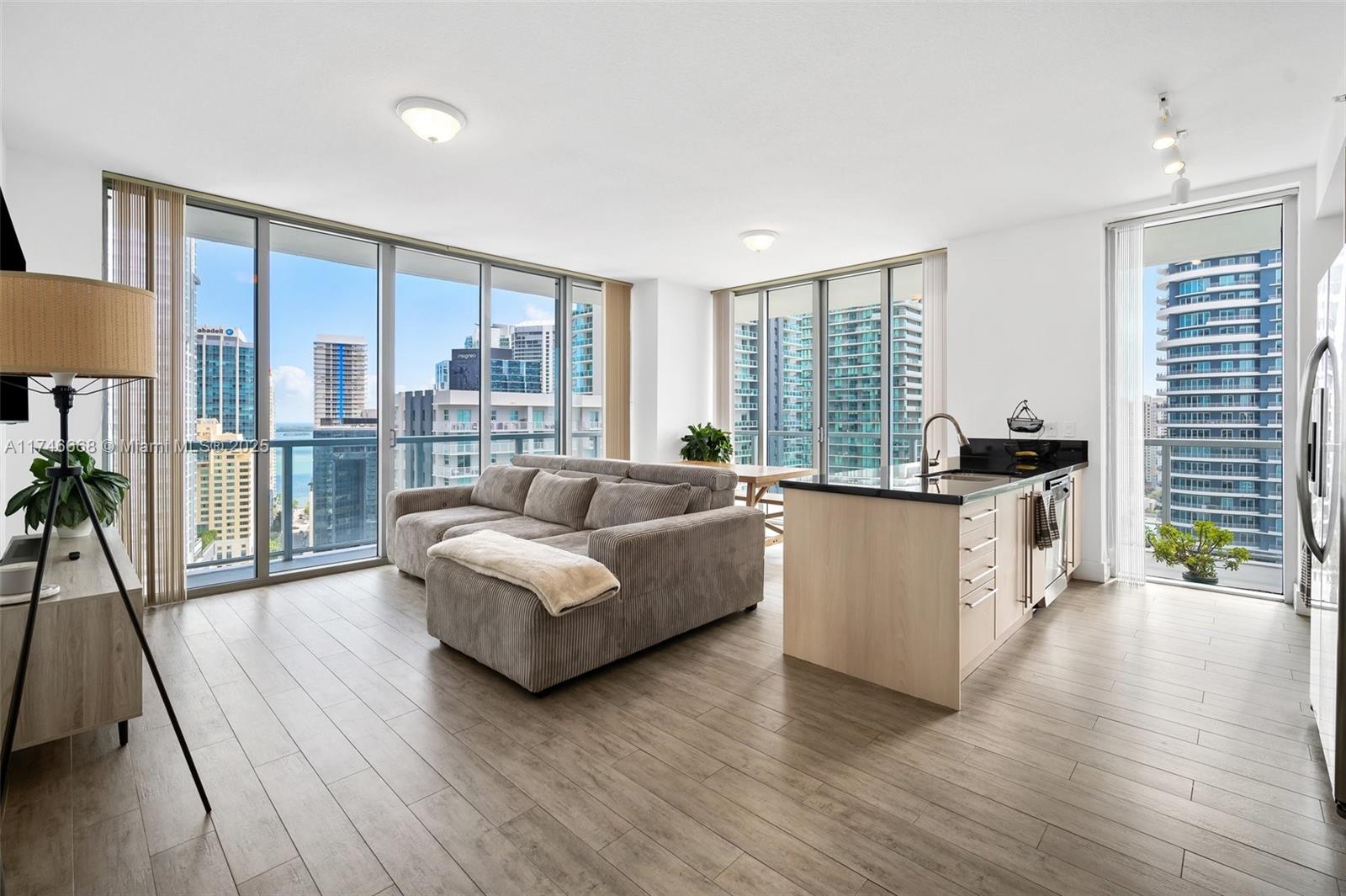 Bright condo living room and kitchen with a gray sectional, kitchen island, and high-rise views.