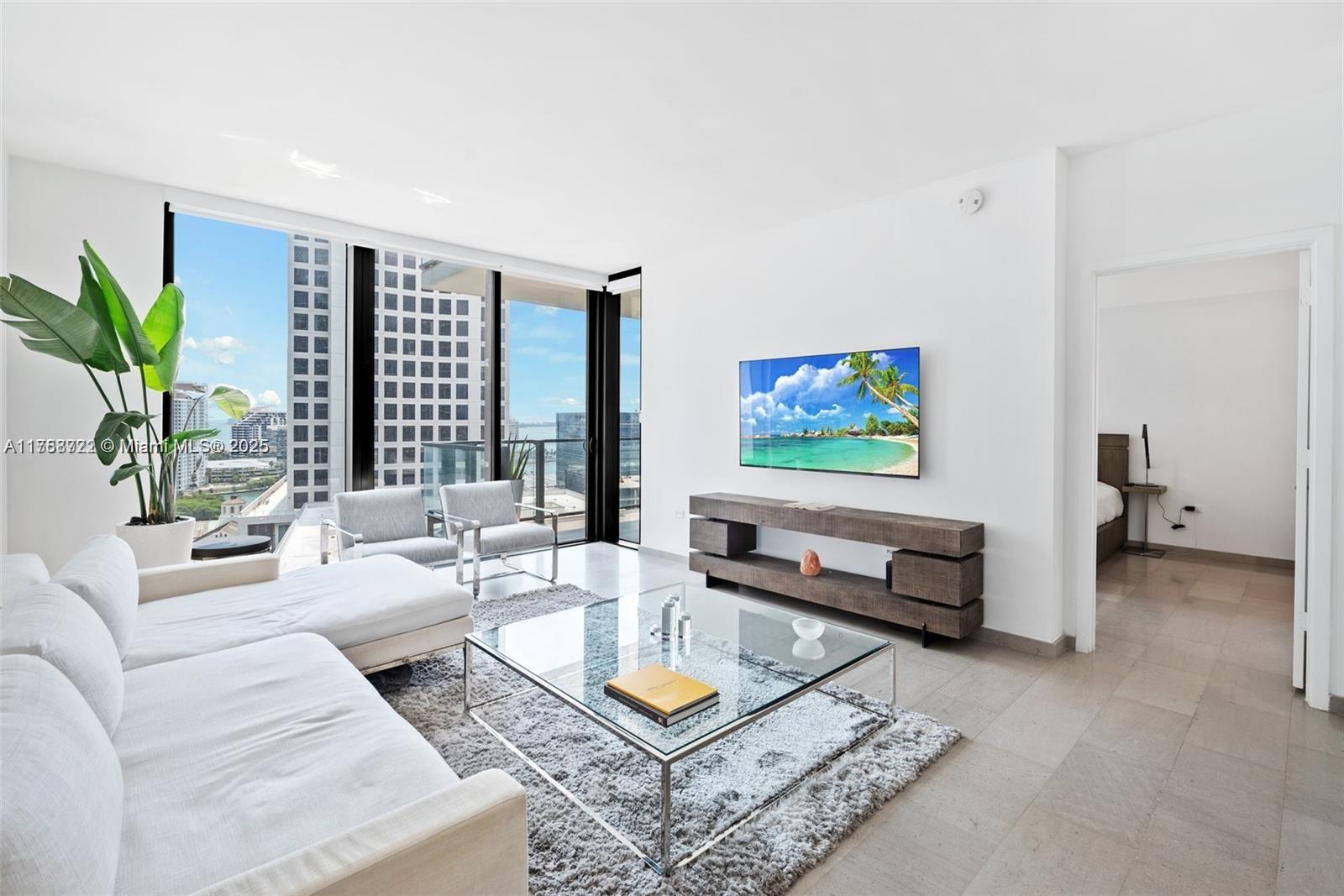 Modern condo living room with a white sectional and floor-to-ceiling windows overlooking Miami high-rises.