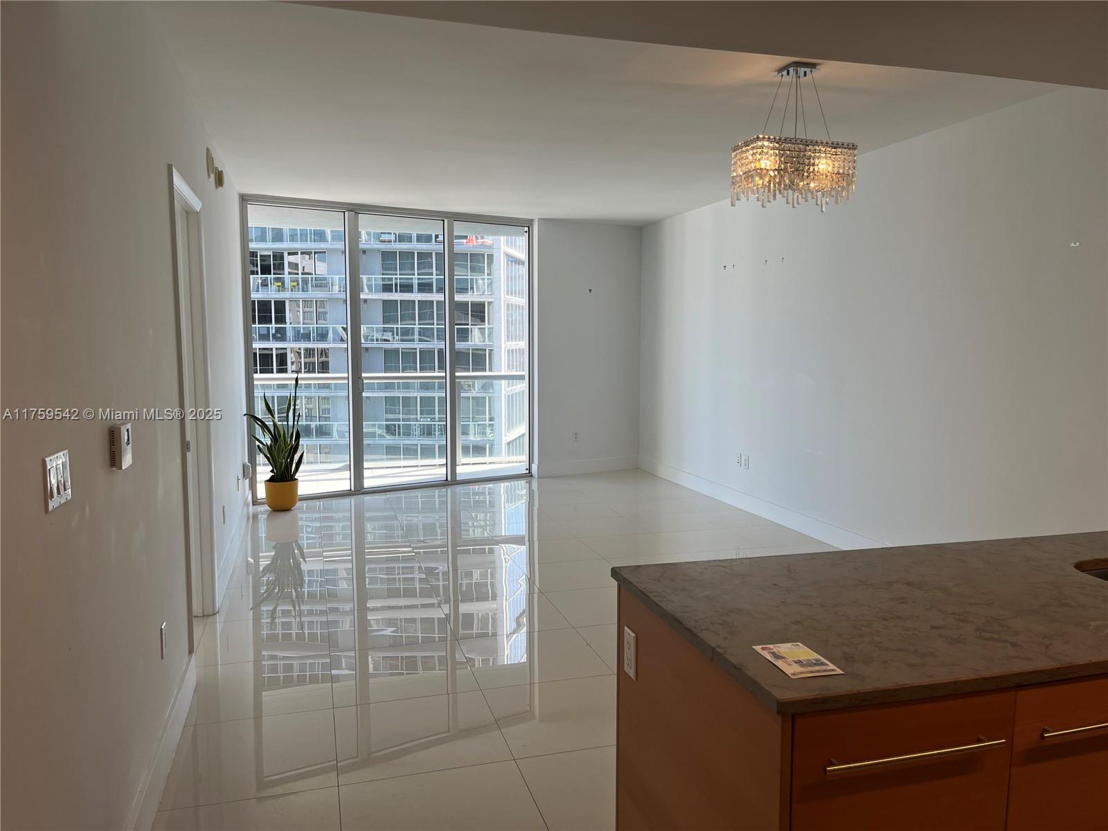 Unfurnished condo living and dining area with glossy floors, a crystal chandelier, and floor-to-ceiling windows.