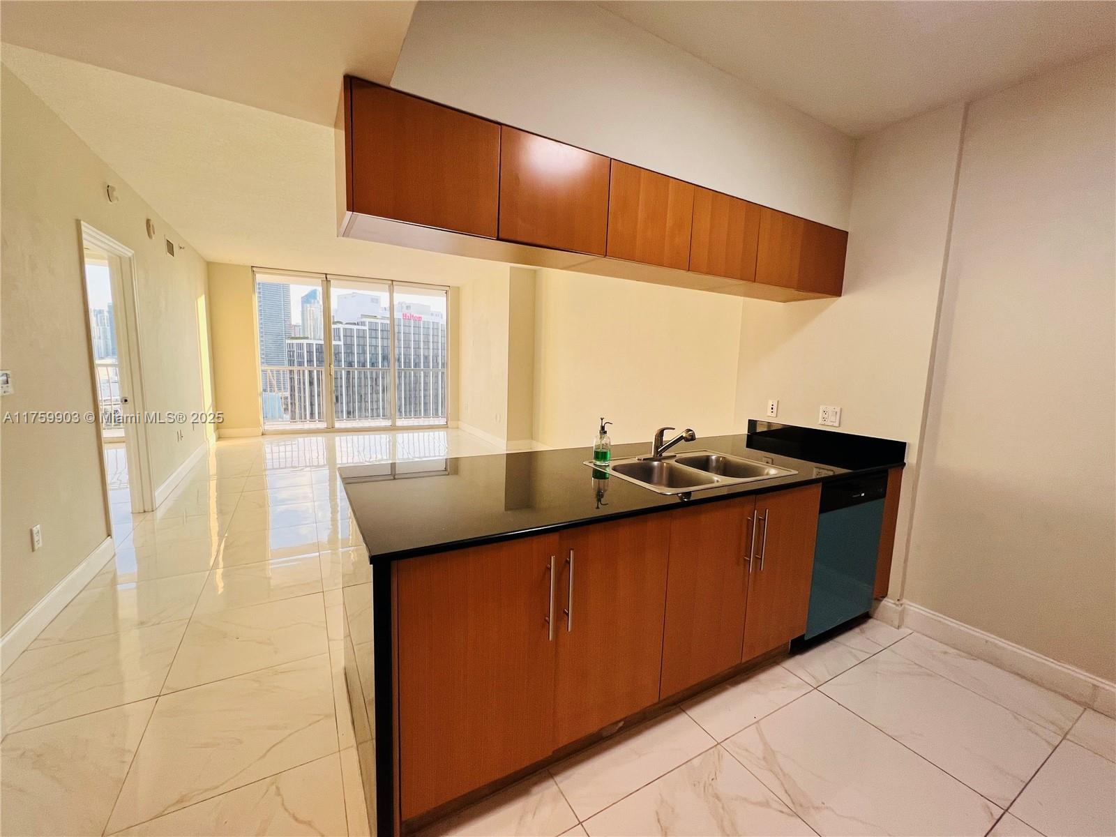 Vacant condo kitchen with wood cabinetry, black stone breakfast bar, and city views through balcony windows.