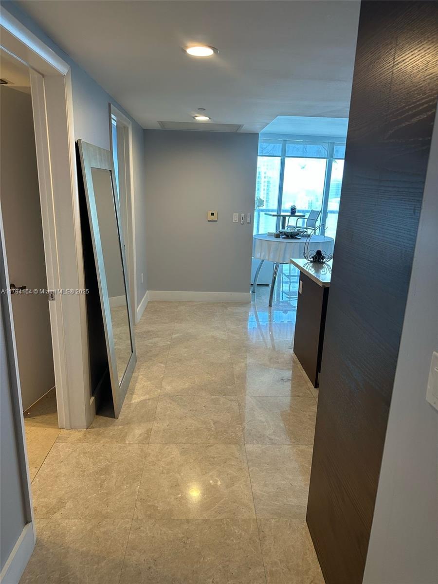 Condo entry hallway with glossy tile floors, a full-length mirror, and dining area beside bright windows.
