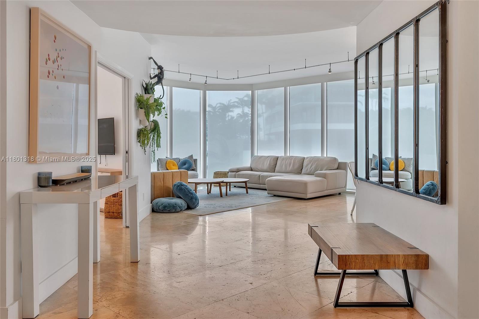 Modern living room with a white sectional, tan chairs, and floor-to-ceiling windows.