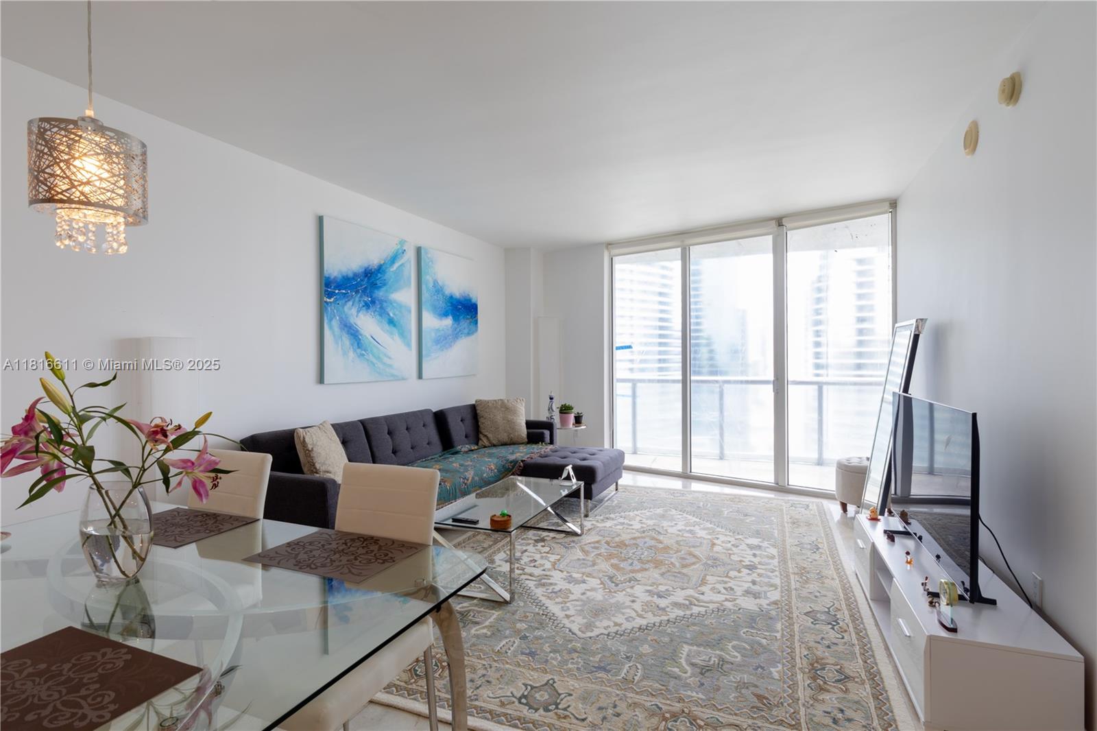 Furnished condo living and dining room with a dark sectional and floor-to-ceiling balcony doors.