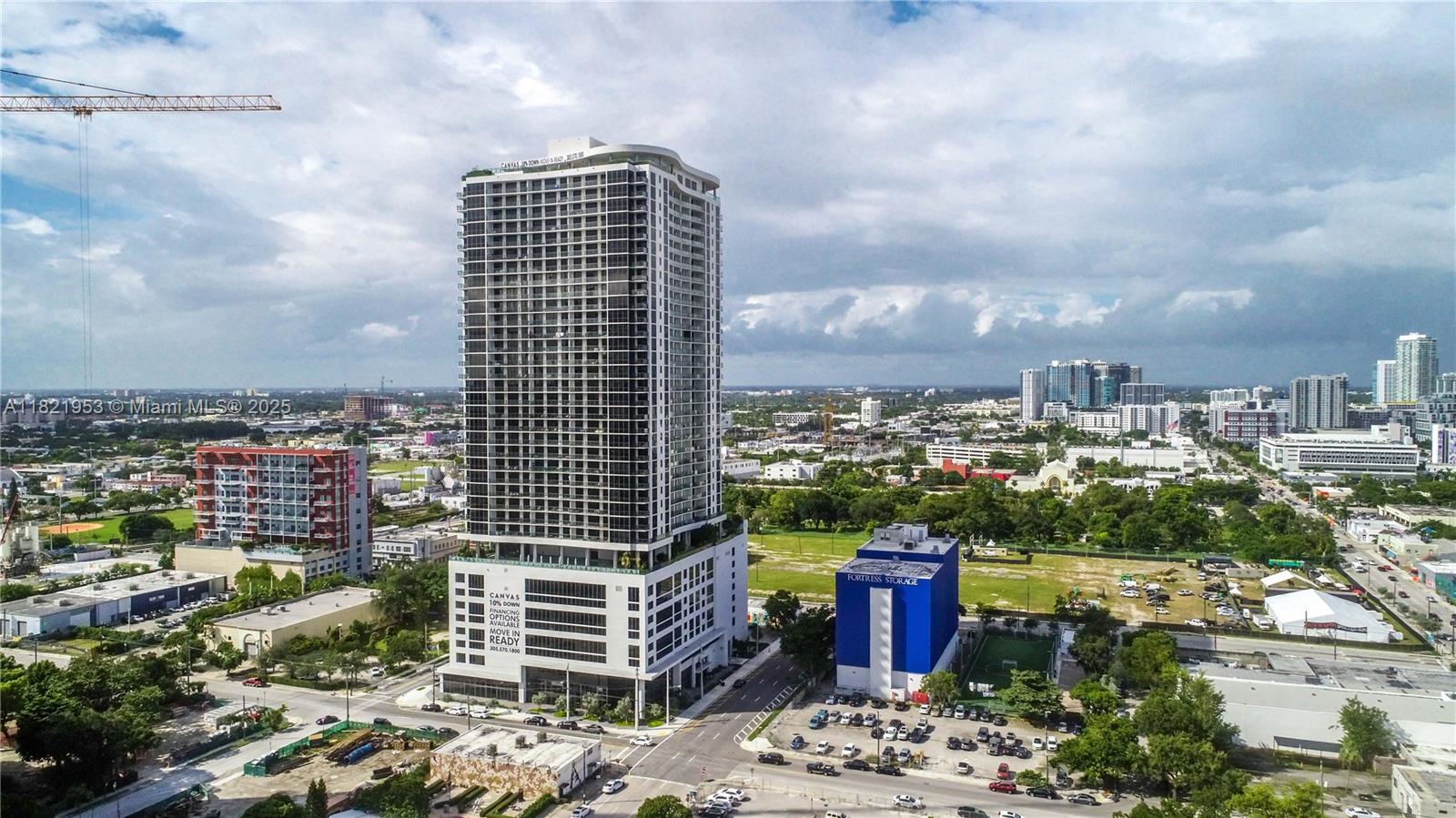 Modern high-rise tower above Miami’s neighborhoods, with the city skyline and a construction crane in view.