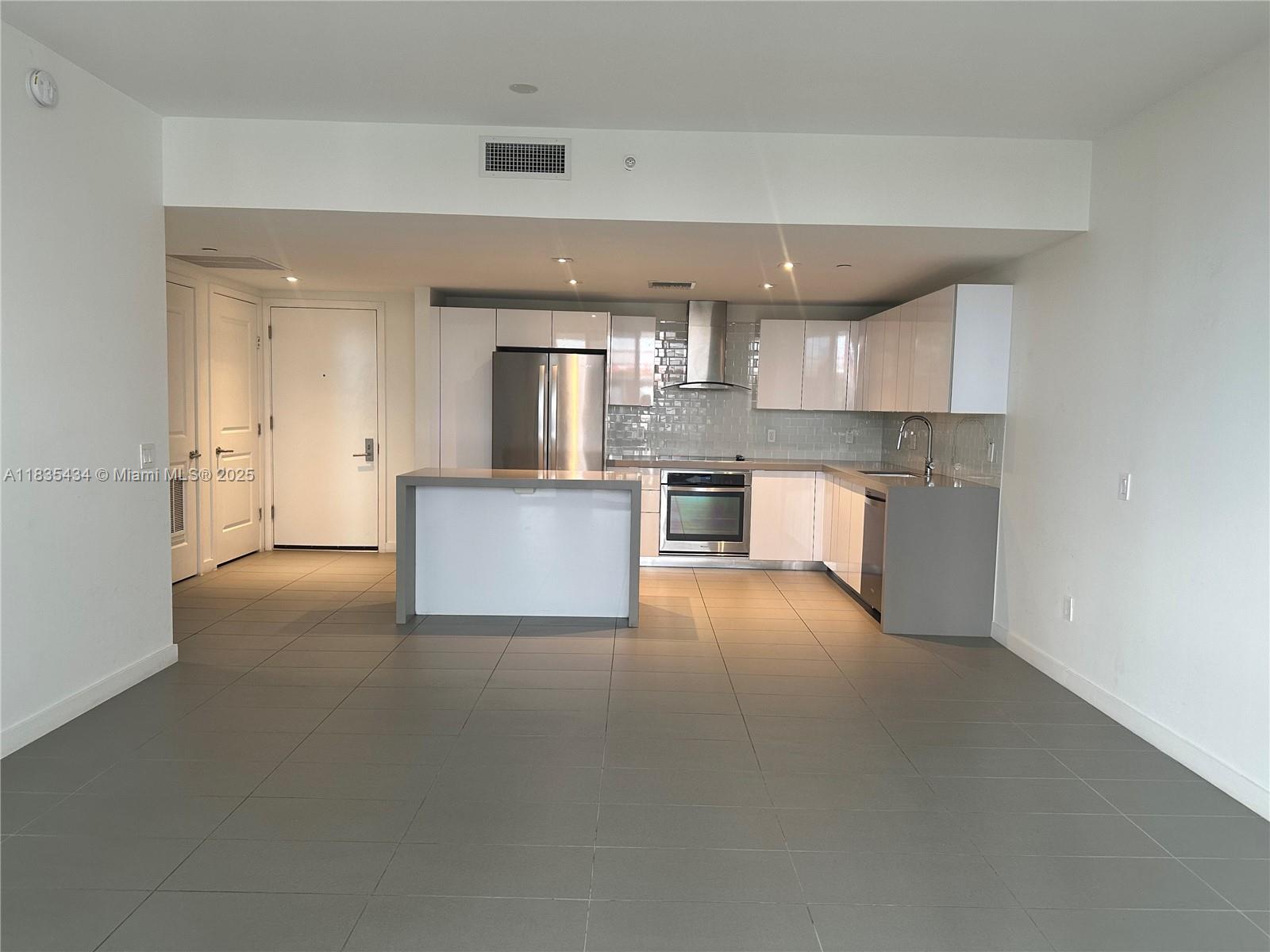 Unfurnished modern kitchen with white cabinets, stainless steel appliances, and a breakfast peninsula.