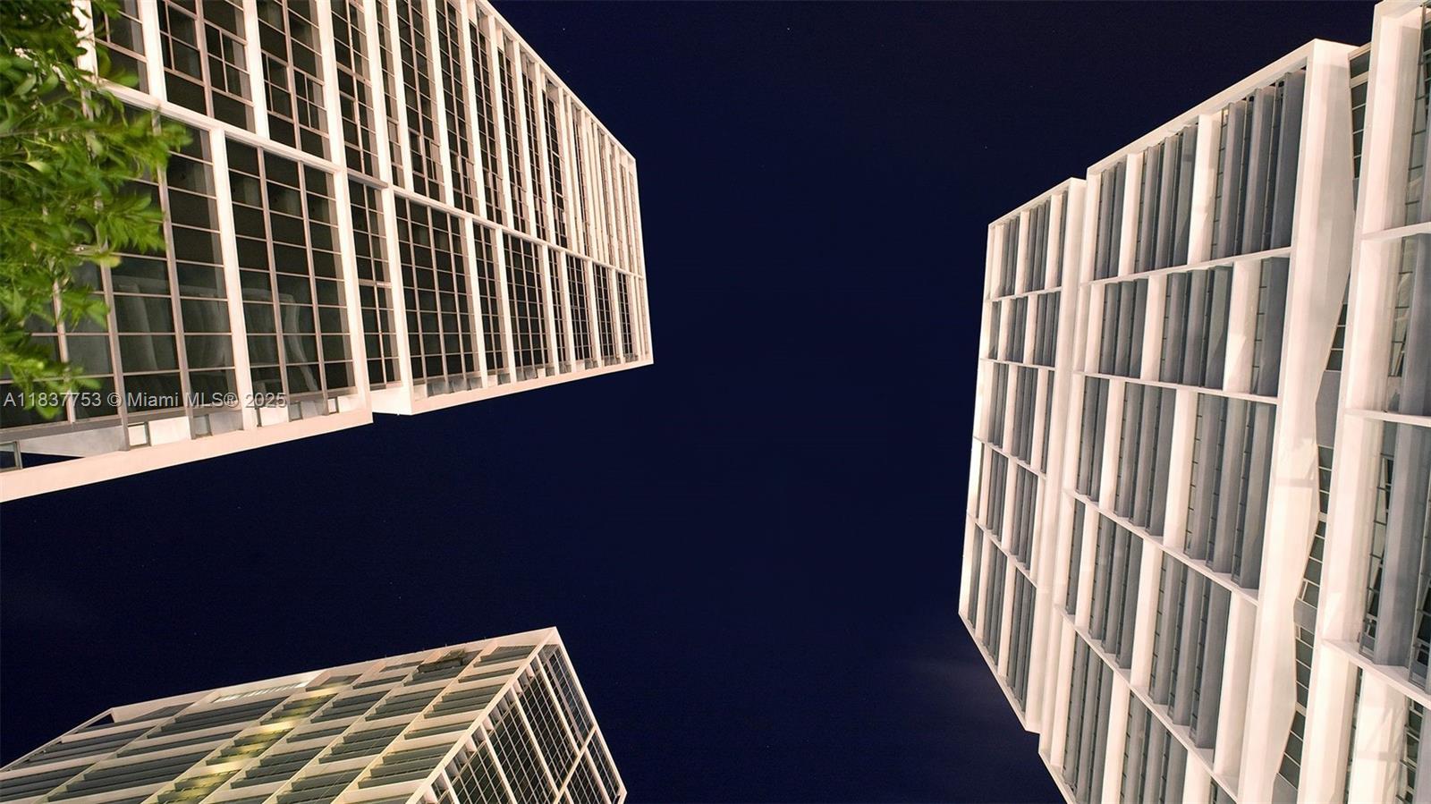 Modern high-rise buildings frame the night sky in an upward view.