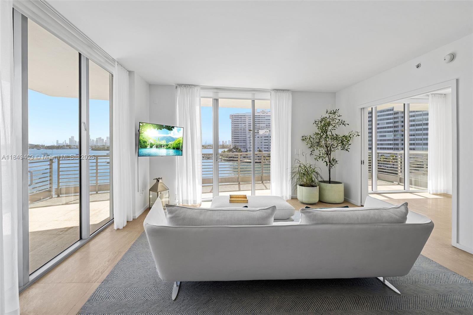 Bright condo living room with floor-to-ceiling windows overlooking water and a distant city skyline.
