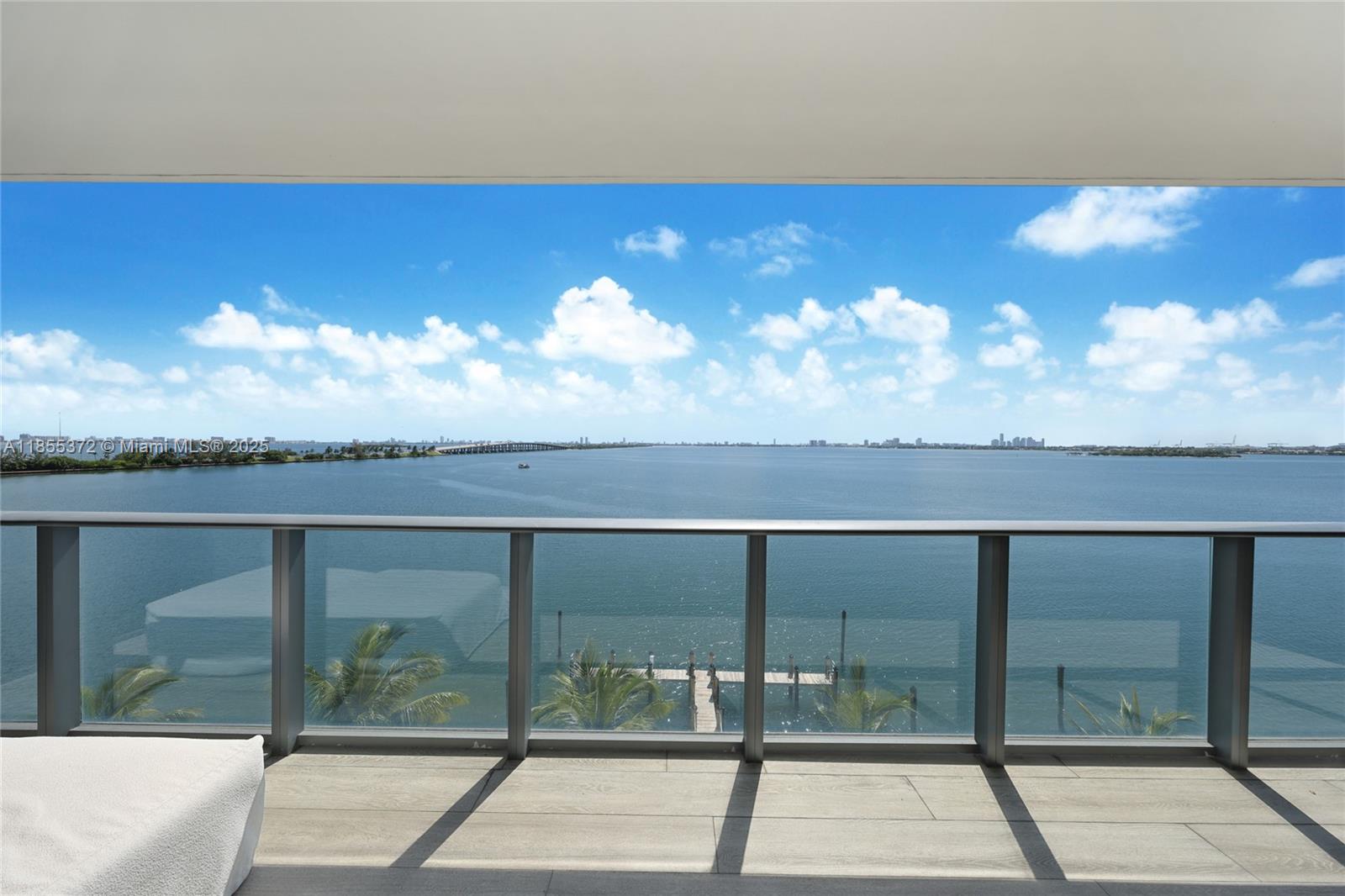 Balcony overlooking Biscayne Bay, with a glass railing, palm trees, and distant Miami skyline.