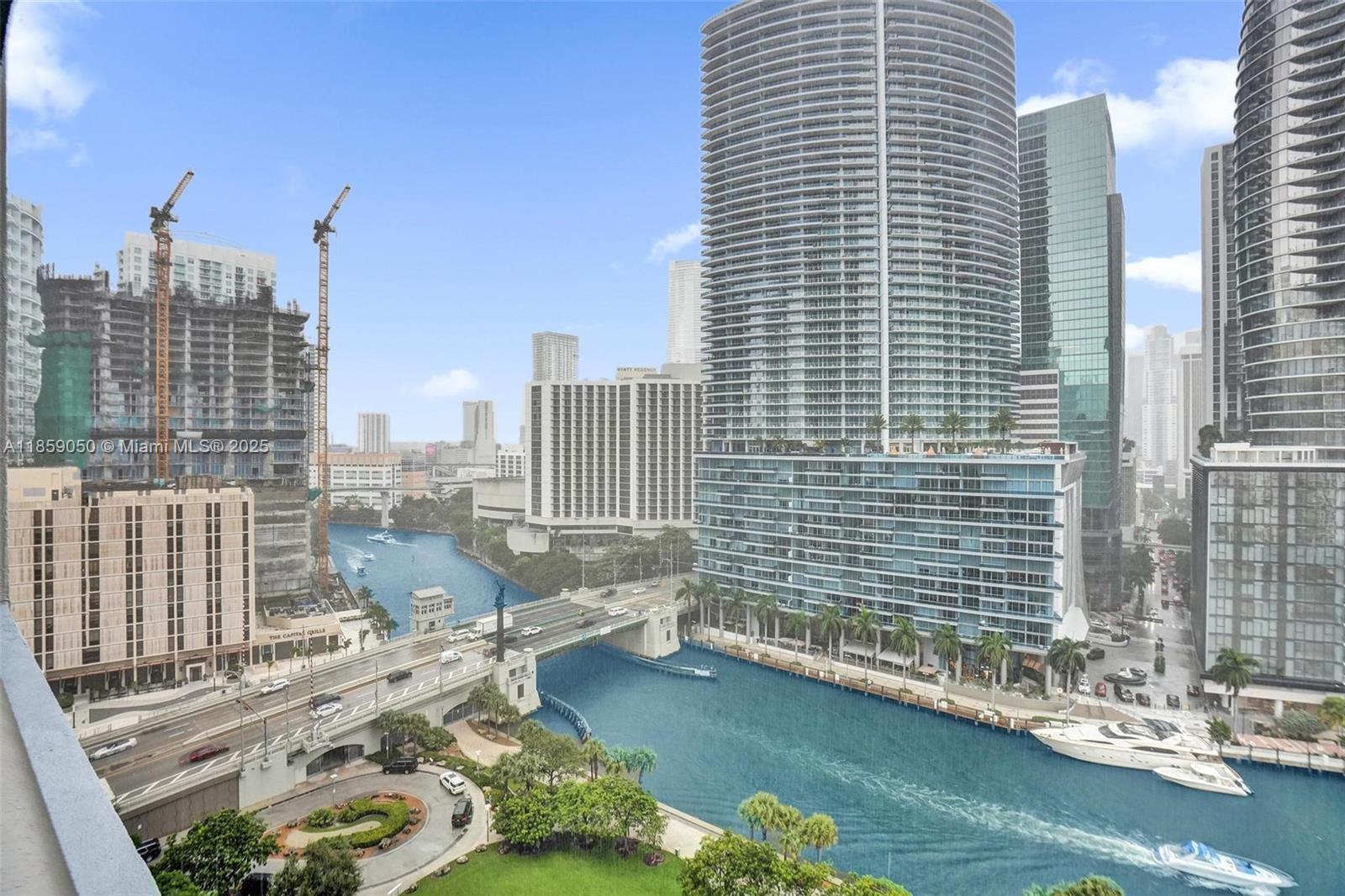 Miami waterfront skyline with high-rises, a canal, boats, and a bridge.