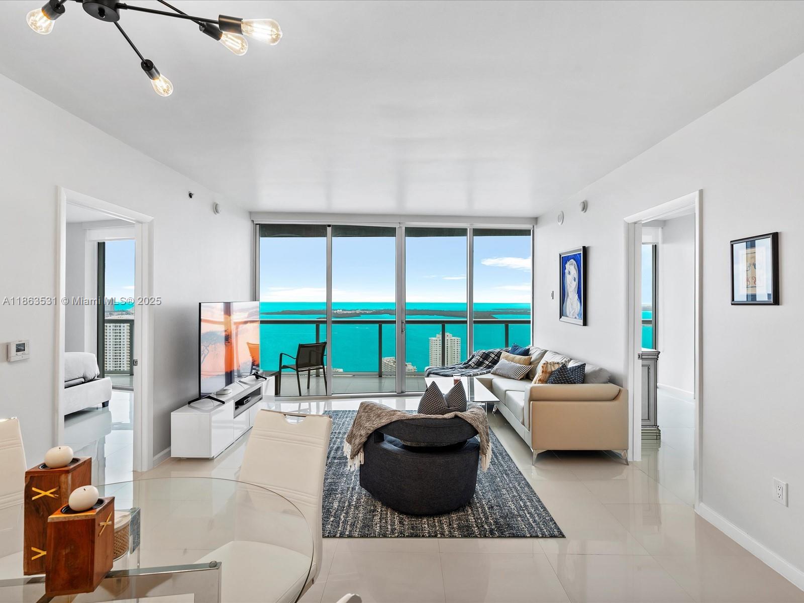 Modern living room with floor-to-ceiling windows overlooking turquoise water and distant buildings.