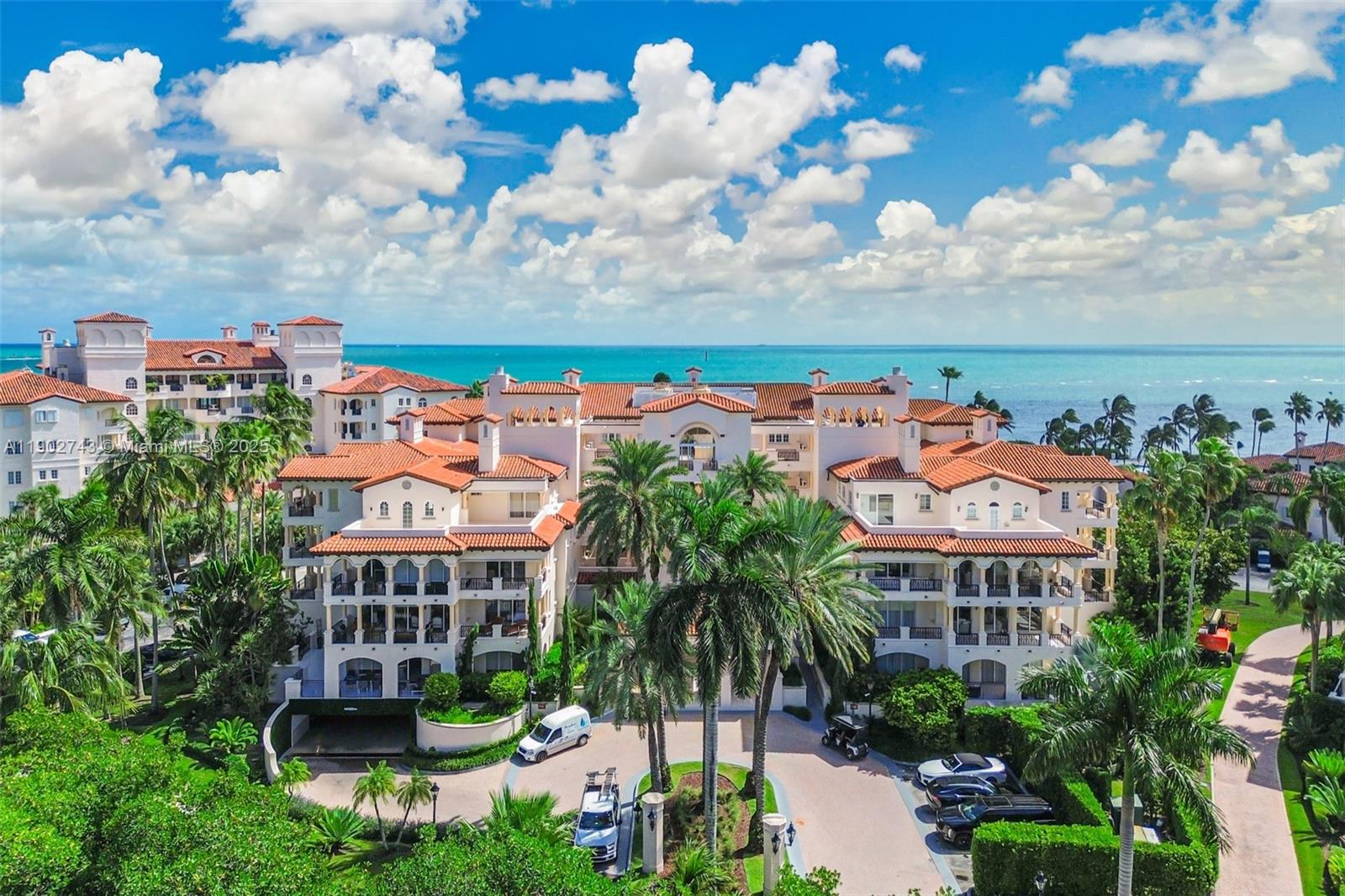 Aerial view of terracotta-roofed beachfront residences, palm trees, and turquoise ocean.
