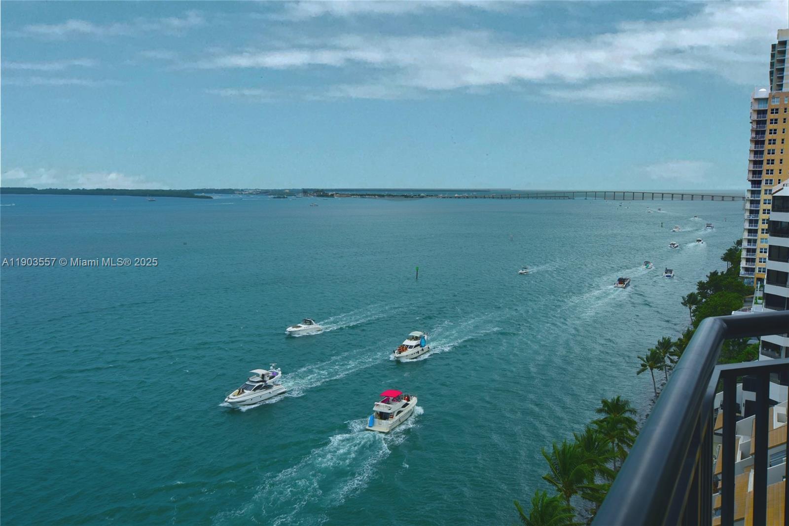 Bay view from a high-rise balcony with motorboats and a distant bridge.
