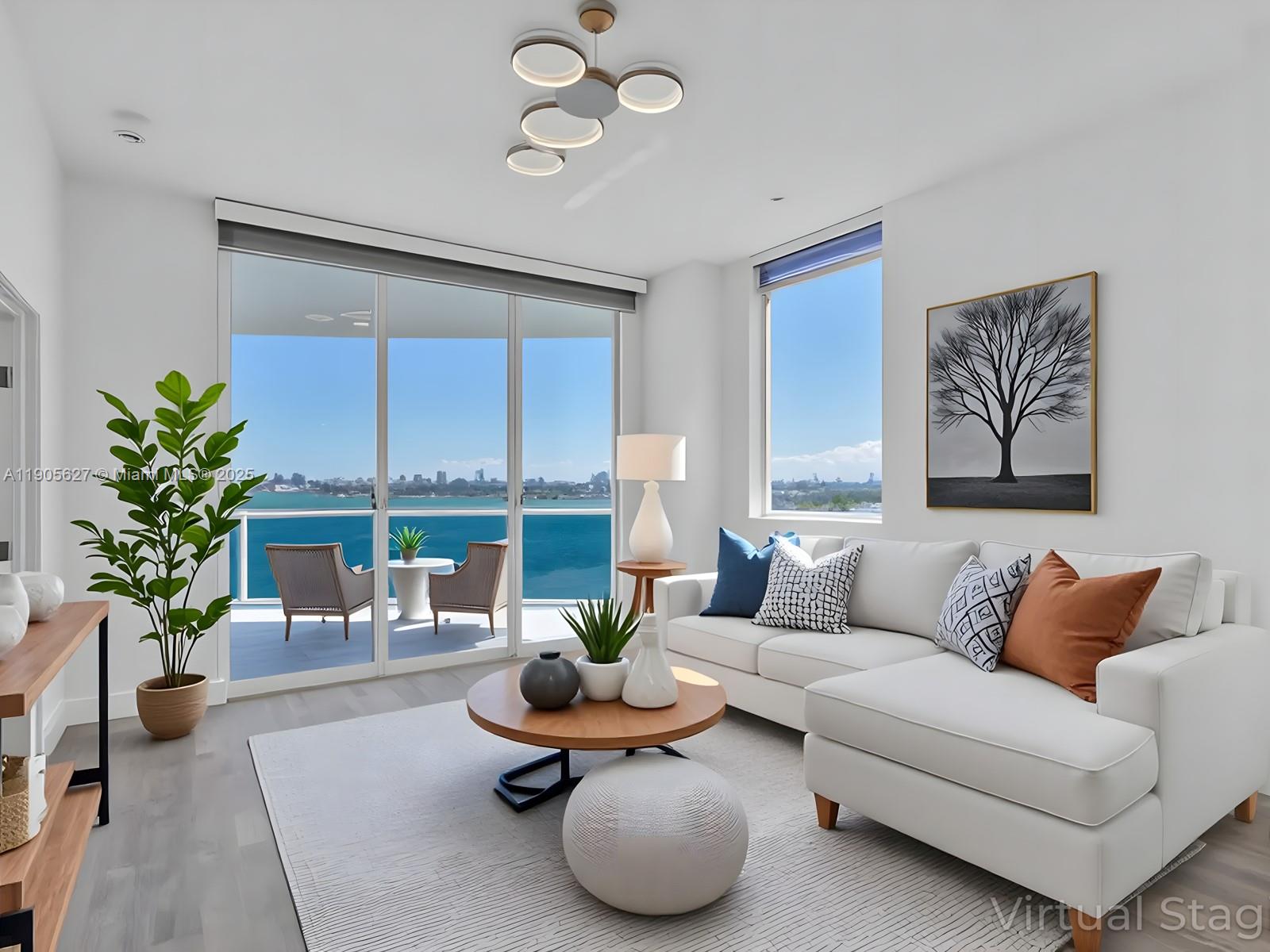 Virtually staged living room with a white sectional and floor-to-ceiling windows overlooking the water.
