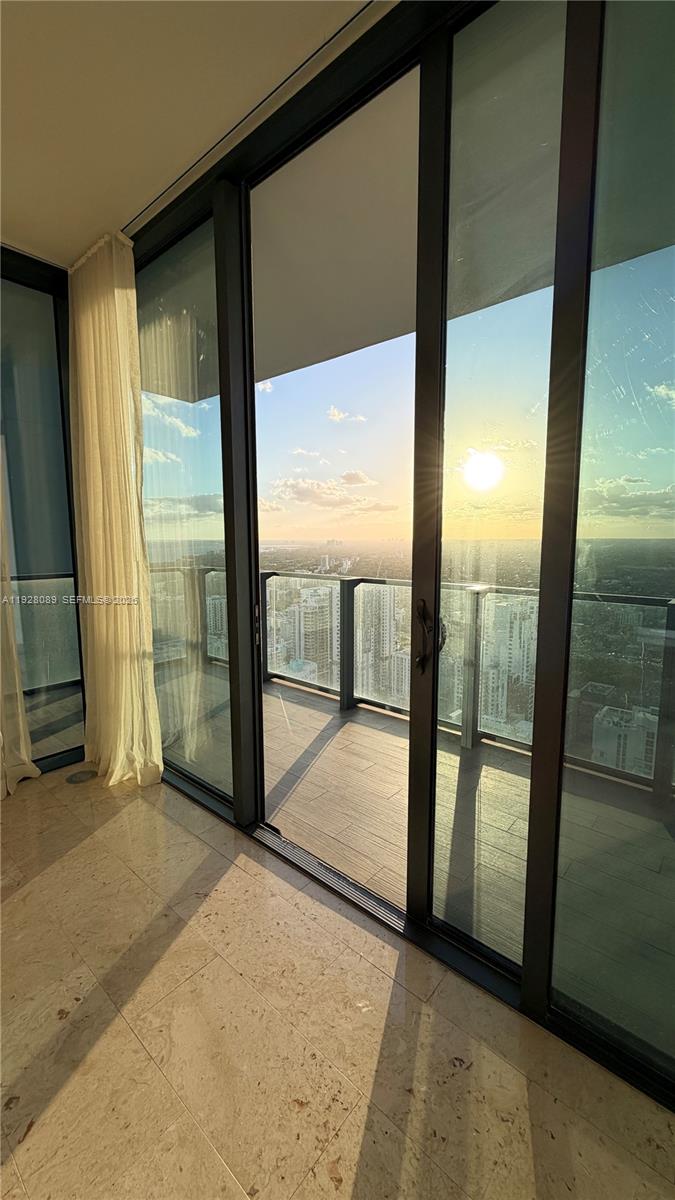 Empty high-rise interior opening to a balcony with floor-to-ceiling glass and a golden-hour city view.