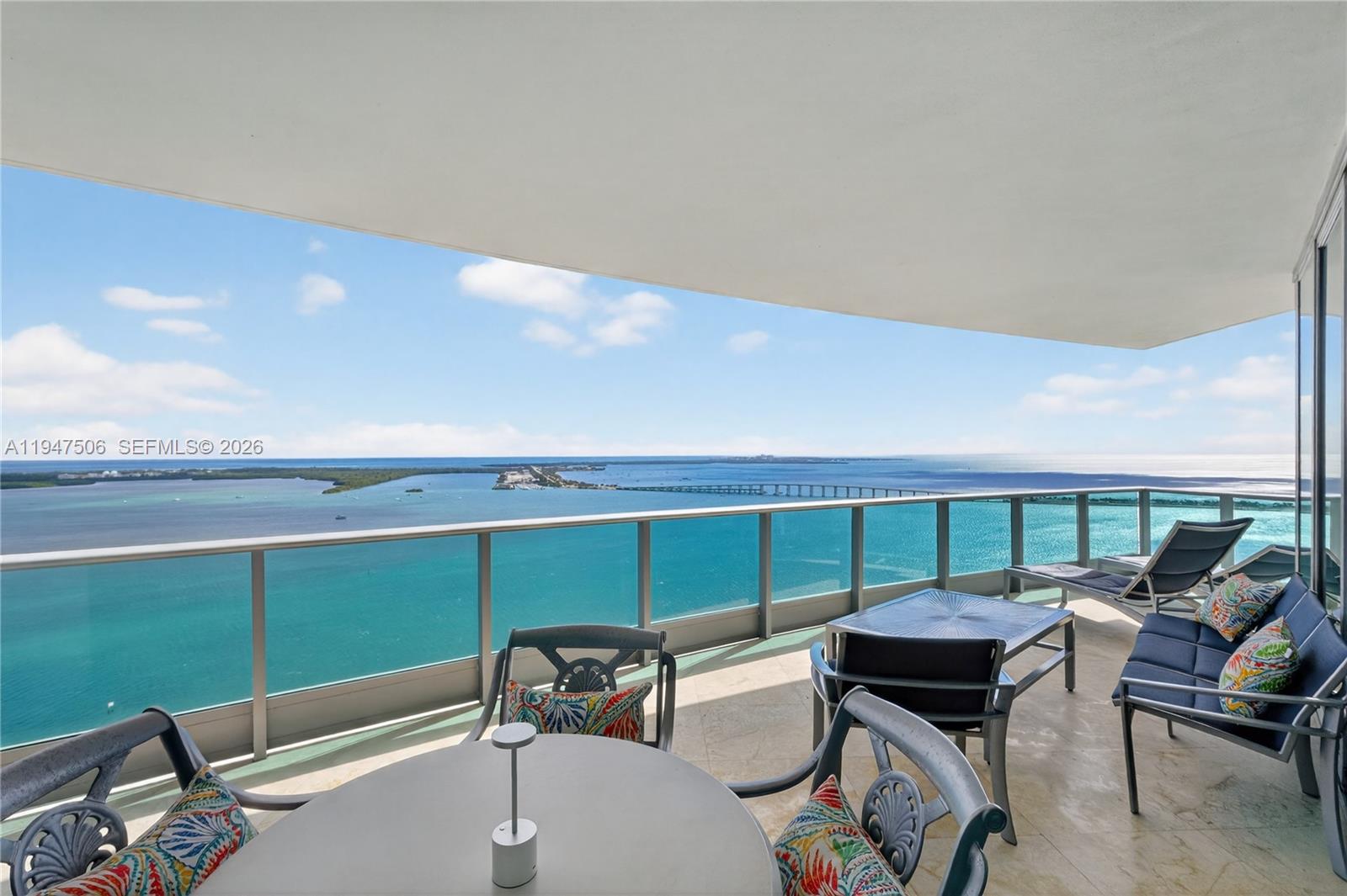 Furnished balcony overlooking turquoise bay water and a distant bridge.