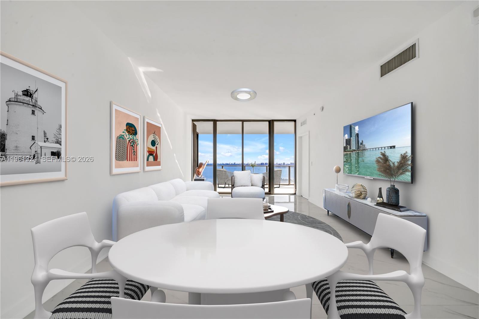 Furnished living and dining room with a white sectional and balcony overlooking water and a city skyline.