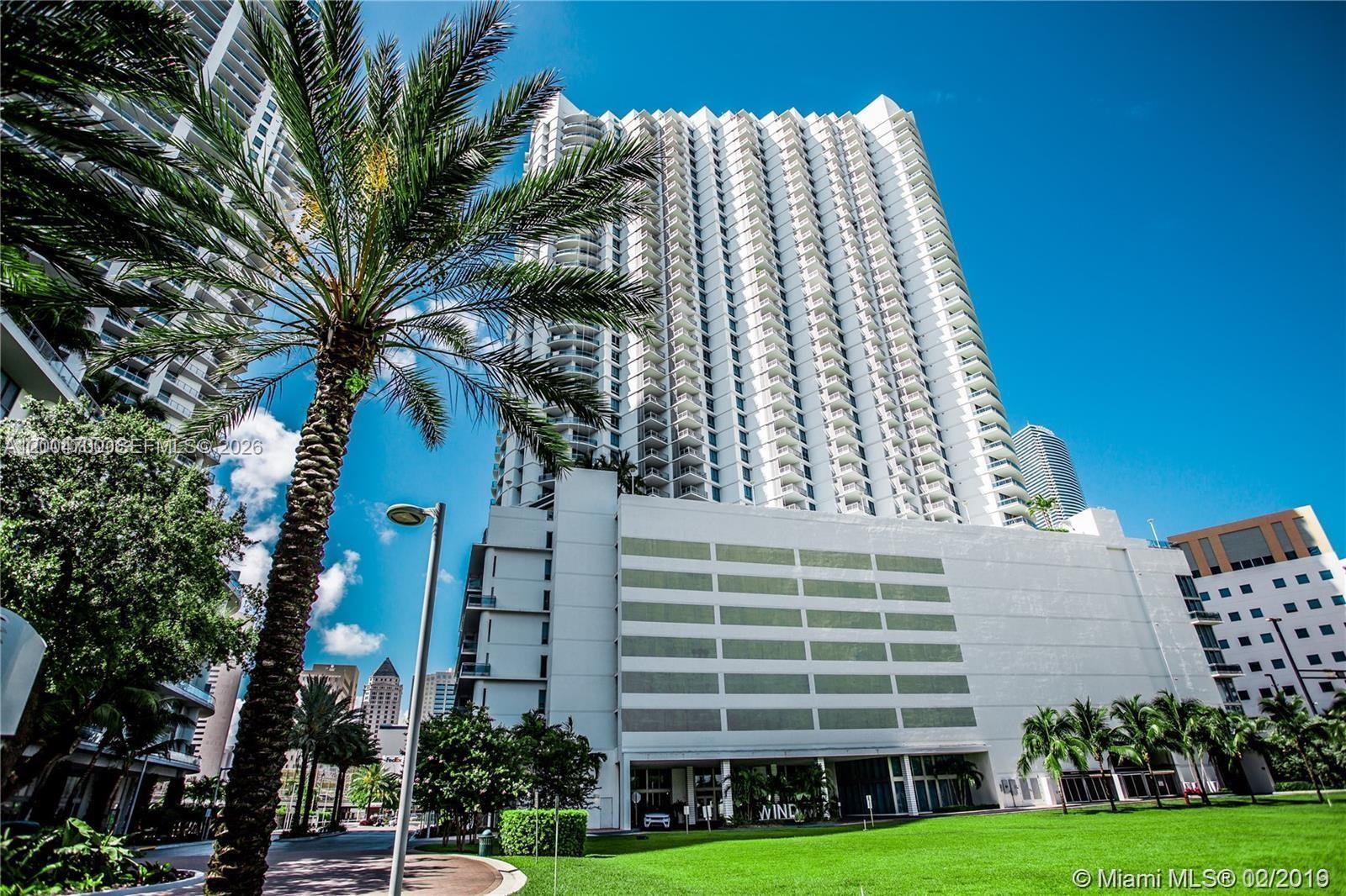 White condominium tower with repeating balconies framed by palm trees and a green lawn.