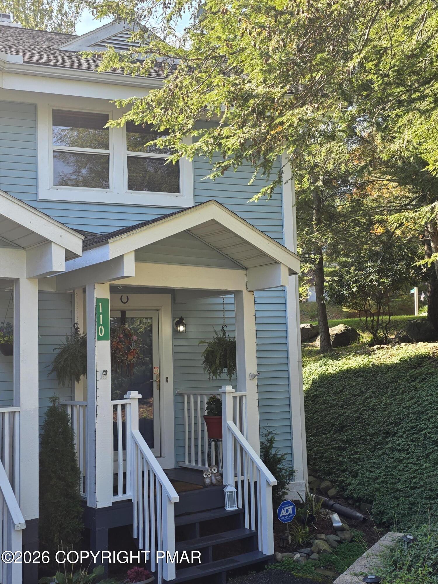 Blue-sided two-story home with a white-trimmed porch beneath mature trees.