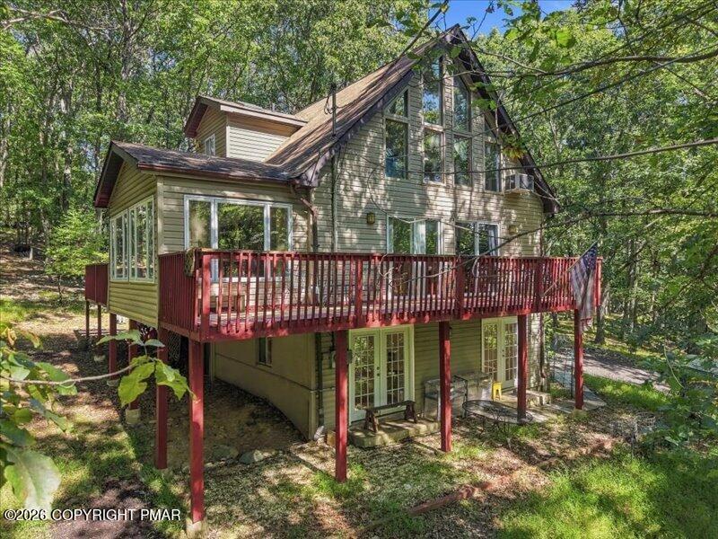 Wooded multi-level house with a large elevated deck and red railings.