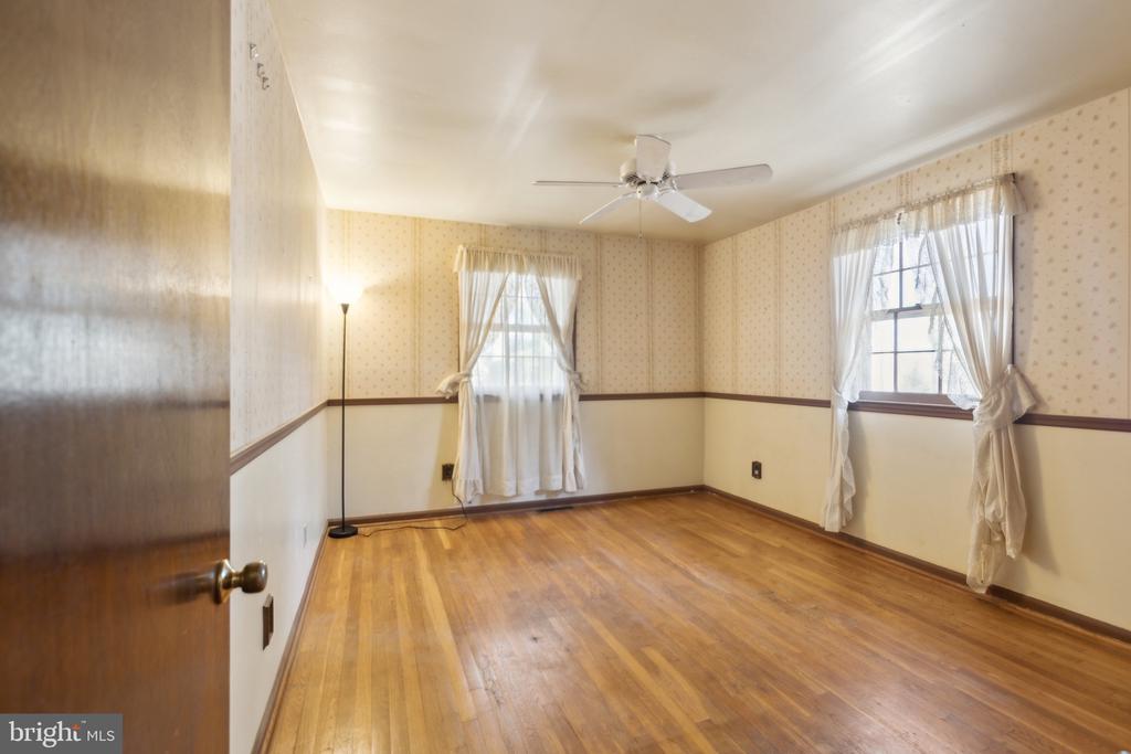Empty bedroom with hardwood floors, two curtained windows, patterned wallpaper, and a ceiling fan.
