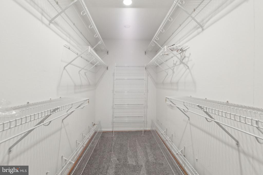 Walk-in closet with white wire shelving on three sides and gray carpet.