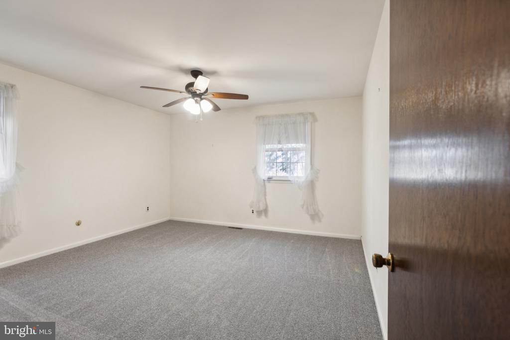 Empty bedroom with gray carpet, two curtained windows, and a ceiling fan with lights.