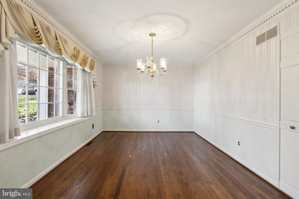 Empty dining room with hardwood floors, chandelier, paneled walls, and large windows with gold drapes.