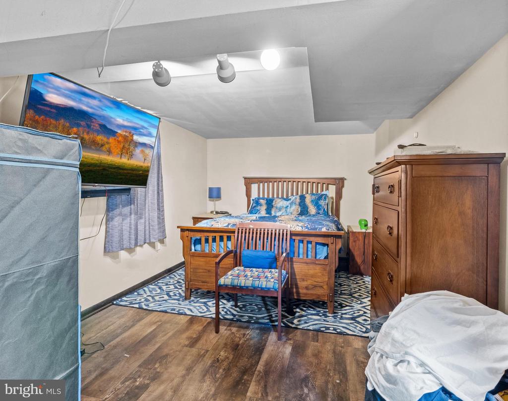 Furnished bedroom with a wooden bed, matching dresser, patterned rug, and wall-mounted television.