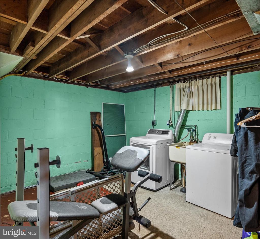 Basement laundry area with exposed ceiling joists, turquoise walls, washer and dryer, and exercise equipment.