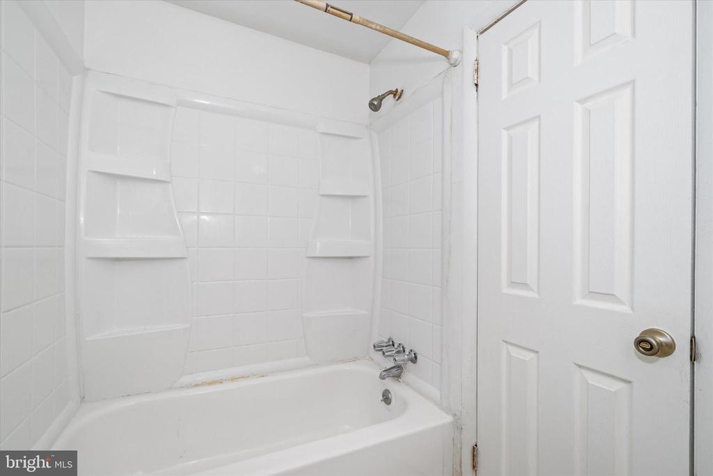 White bathtub with tiled shower surround, built-in shelves, chrome fixtures, and a paneled door.