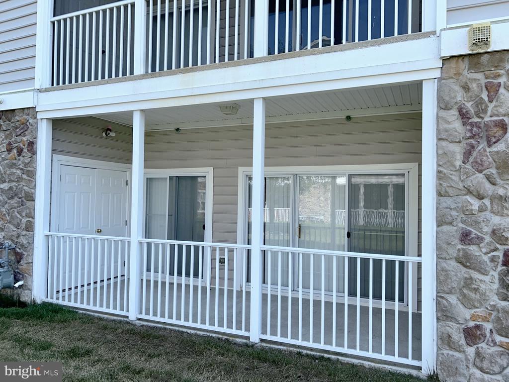 Covered patio with white railings, sliding glass doors, and stone exterior walls.