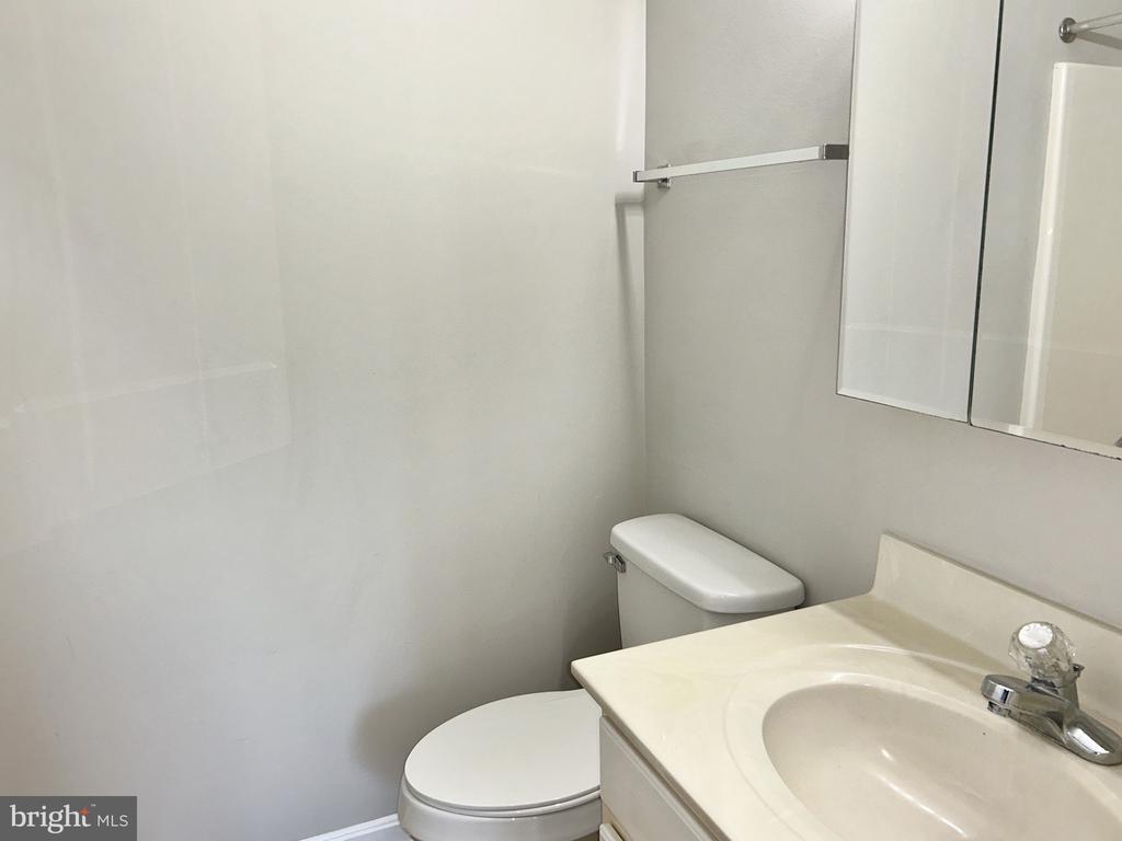 Empty bathroom with a white toilet, cream vanity, oval sink, and wall mirror.