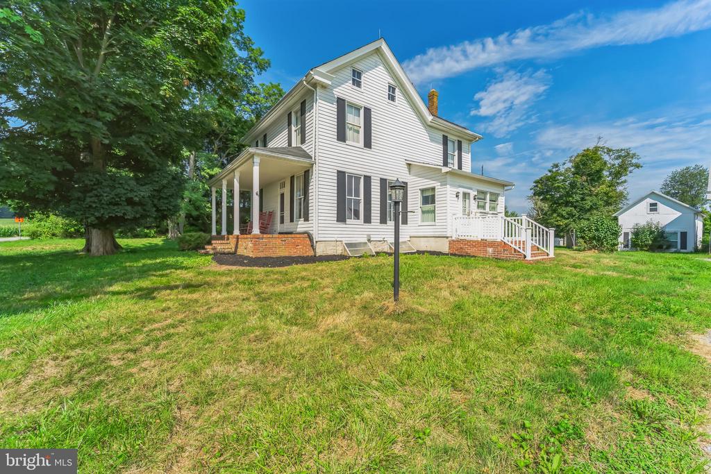 White two-story house with a covered porch, grassy lawn, and small detached outbuilding.
