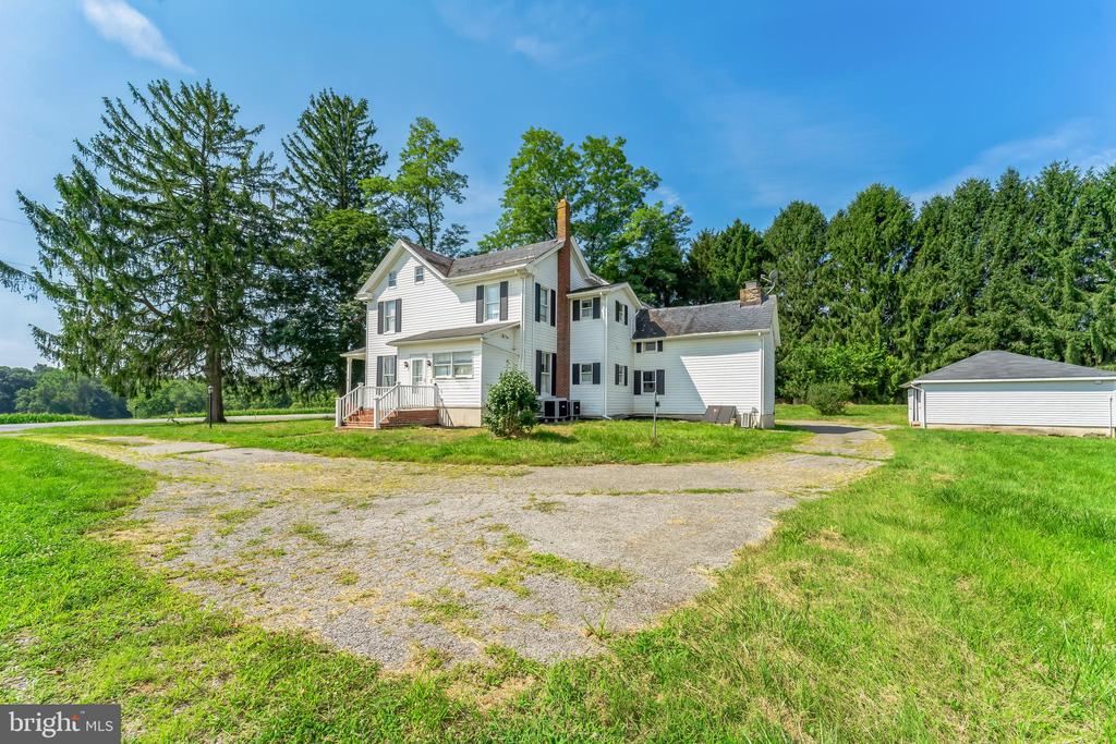 White two-story house with a brick chimney, gravel driveway, and detached outbuilding.
