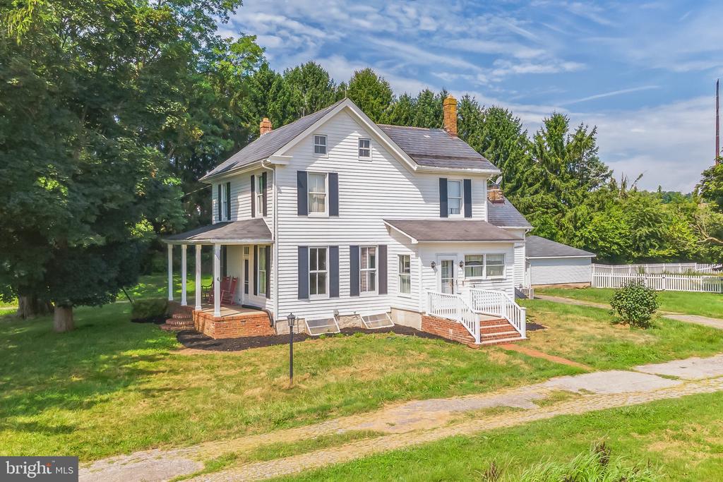 White two-story home with gray shutters, a covered porch, brick steps, and a fenced yard.
