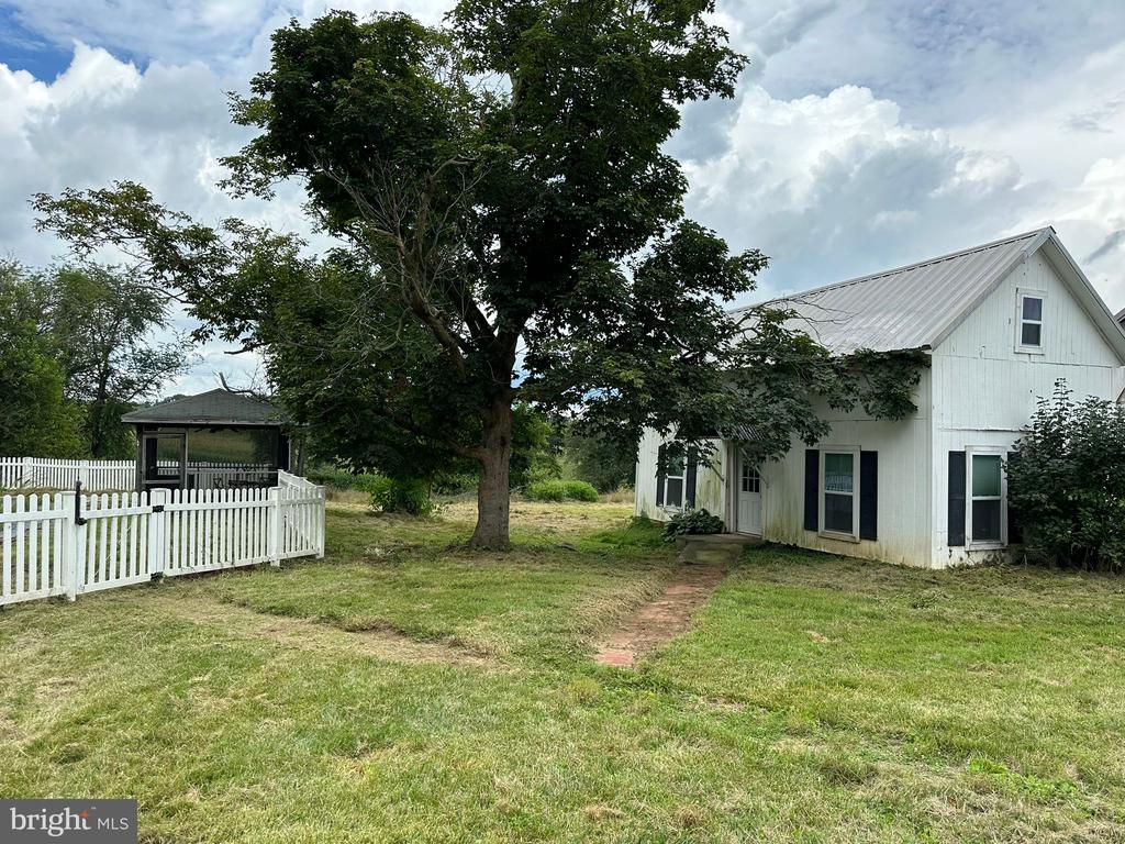 White house with a metal roof, large shade tree, and fenced lawn beside a gazebo.
