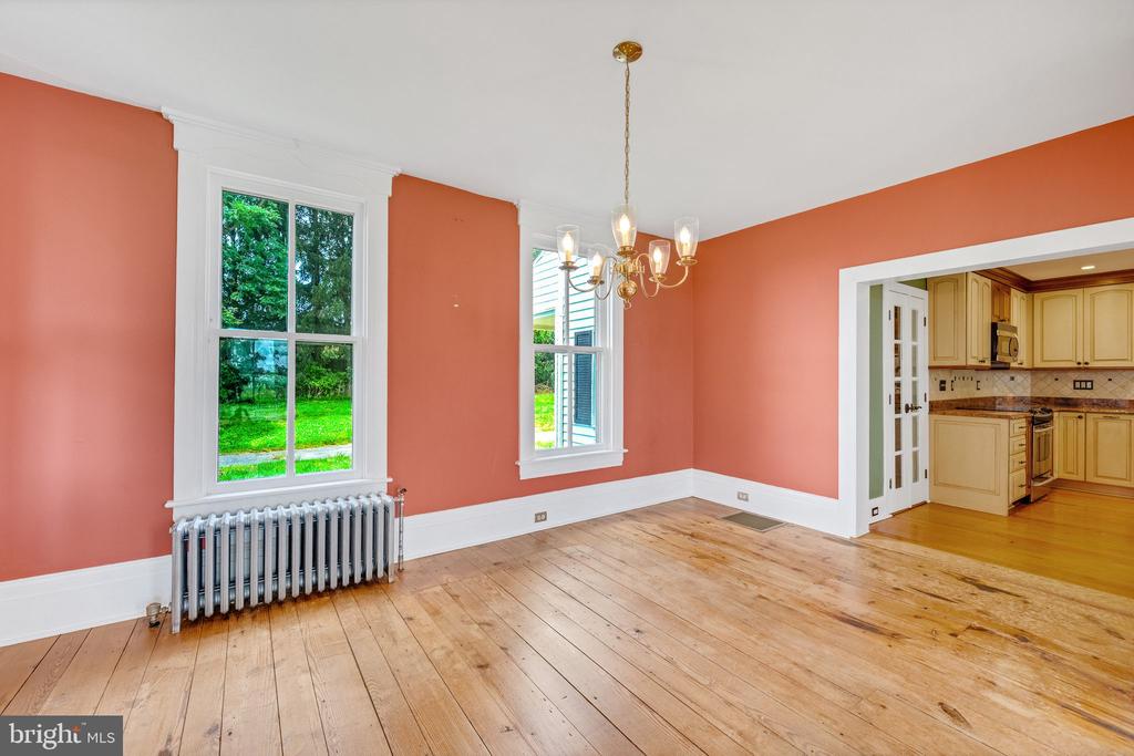 Empty dining room with coral walls, wide-plank wood floors, and a chandelier beside the kitchen.