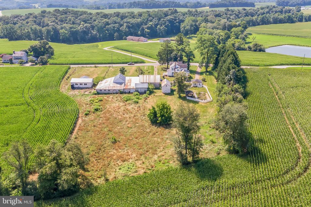 Aerial farm property amid crop fields, with a farmhouse, outbuildings, and pond.