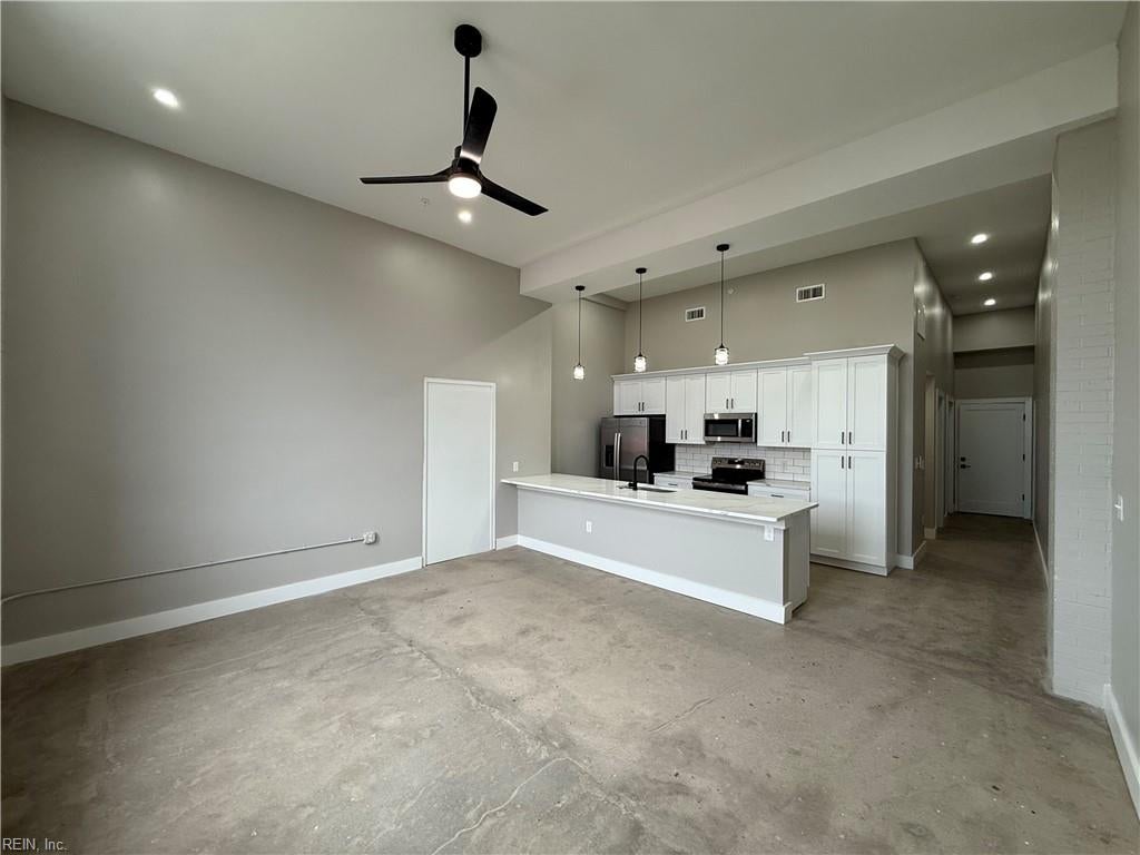 Open kitchen and living area with a large island, white cabinetry, and concrete floors.