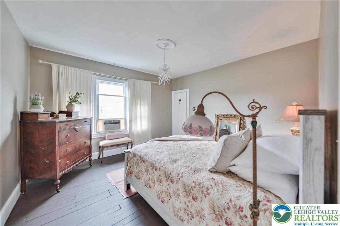 Bedroom with a floral quilt, dark wood dresser, and chandelier.