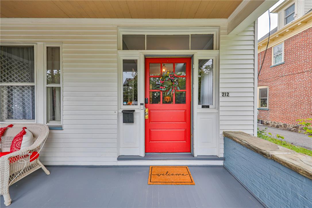 Front porch with a bright red wreath-decorated door, white siding, and a wicker chair.