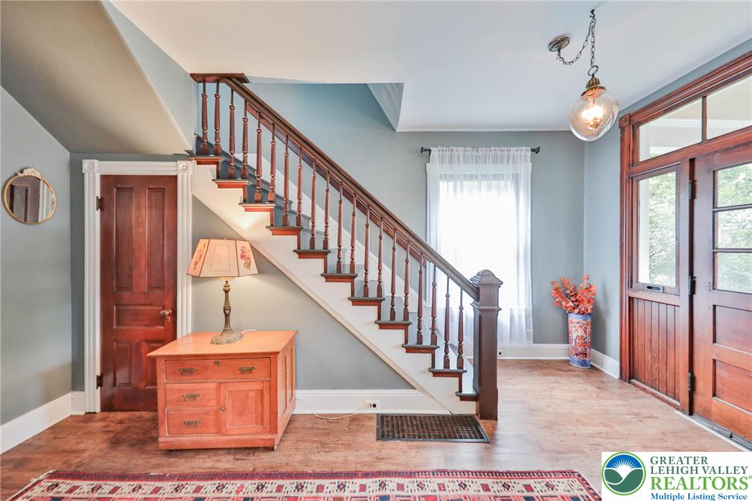 Entryway with a dark wood staircase, paneled front door, tall windows, and hardwood flooring.