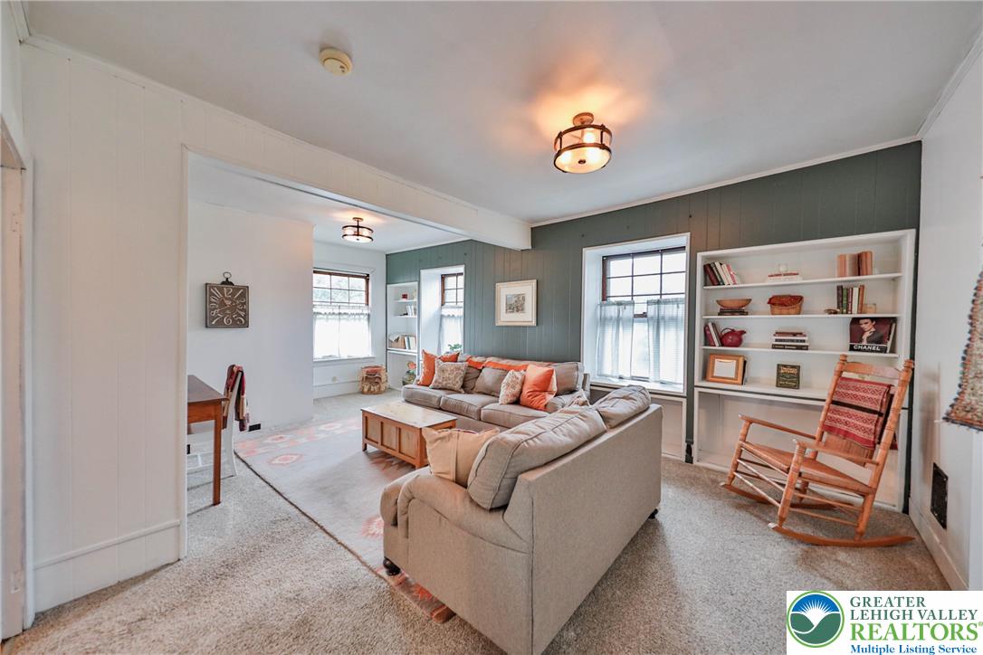 Living room with a gray sectional, green paneled walls, built-in bookshelves, and a wooden rocking chair.