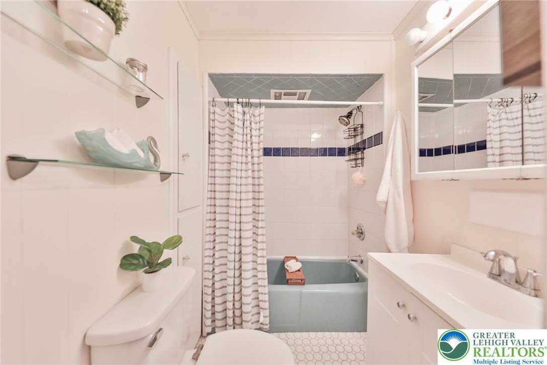 Bathroom with a pale blue bathtub, striped shower curtain, and mirrored vanity.