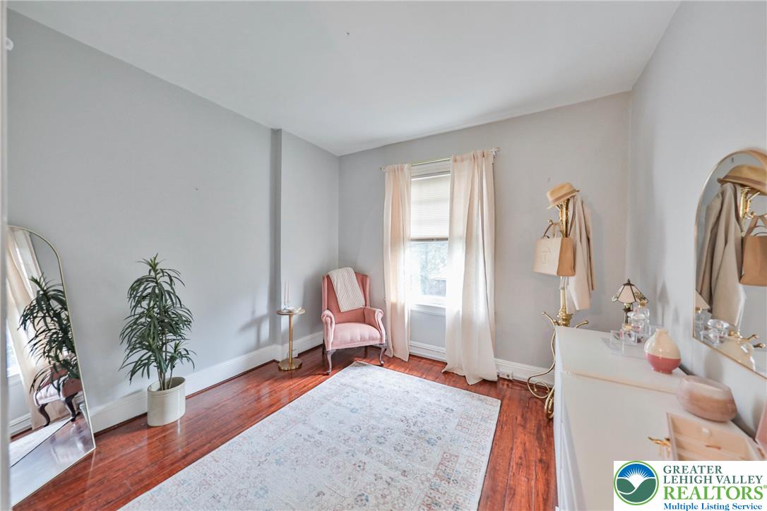 Bedroom with polished hardwood floors, a pink chair, and a white dresser beside a curtained window.